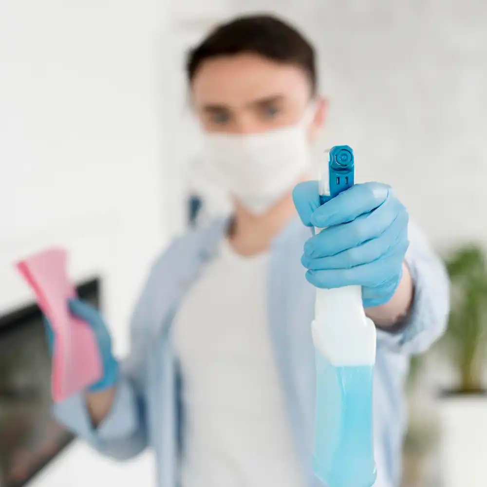 Male professional cleaner in mask and gloves holding disinfectant spray — Busy B Cleaning’s sanitisation services in Australia